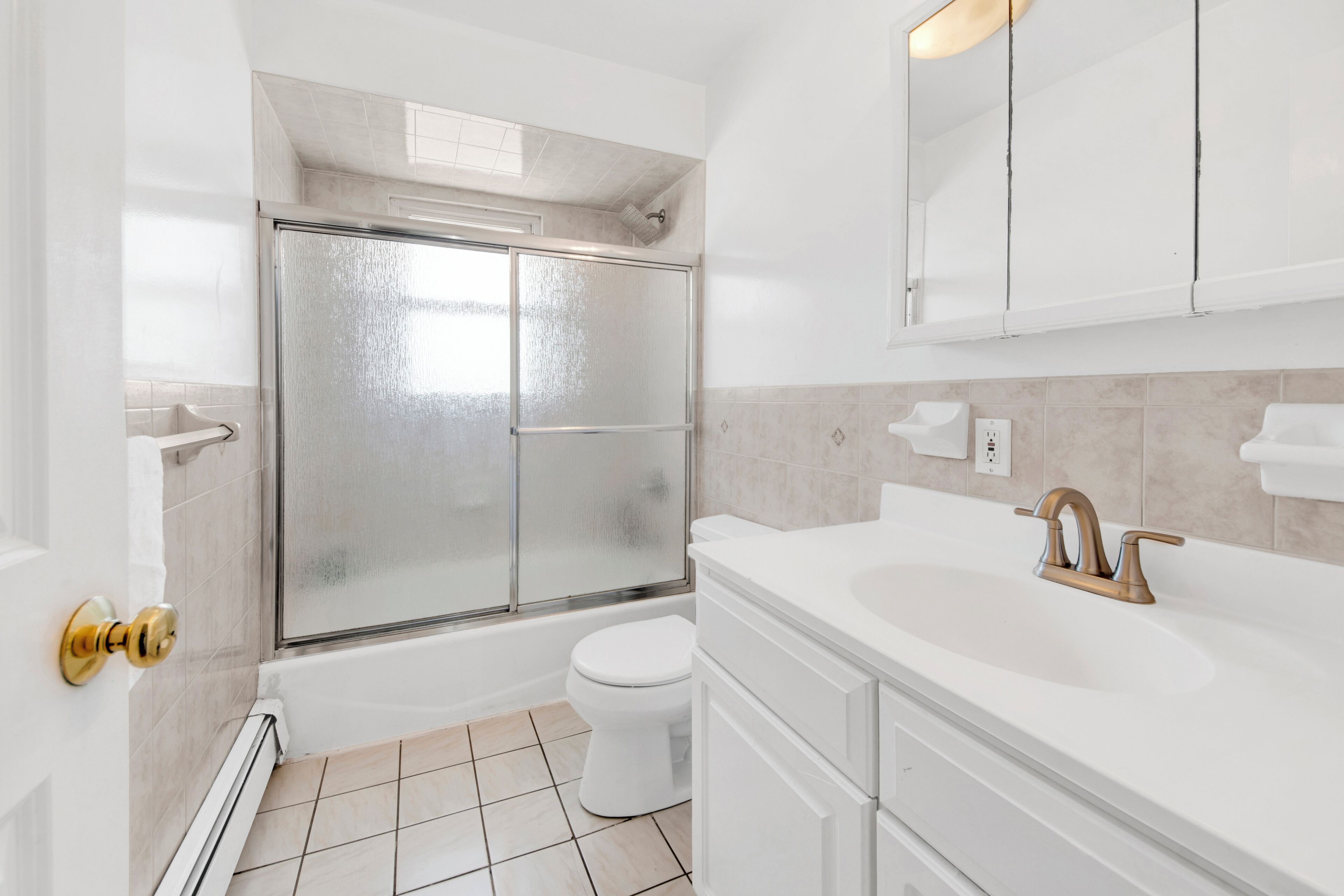 Une salle de bain dotée d’une douche à parois de verre, de toilettes blanches et d’un lavabo avec un robinet doré.