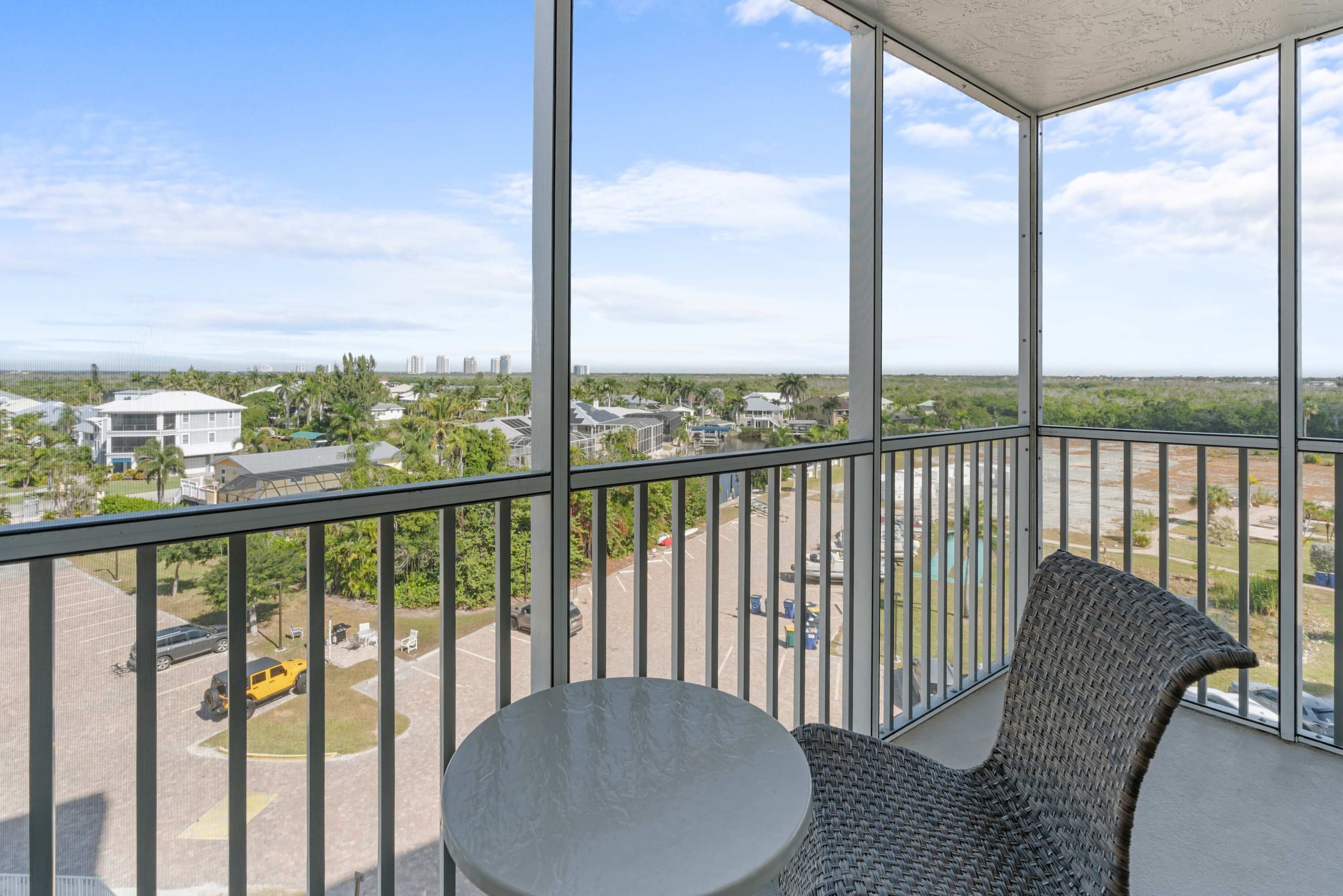 Een balkon met uitzicht op een woonwijk, een ronde tafel en een rieten stoel.