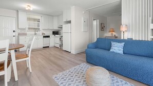 Moderni keittiö, jossa on valkoiset kaapit, ruokapöytä tuoleineen, sininen sohva ja kuviollinen matto.