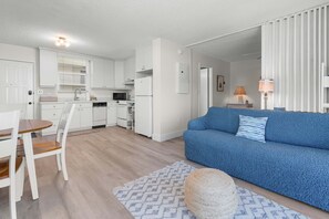 A modern kitchen with white cabinets, a dining table with chairs, a blue sofa, and a patterned rug. - Cozy Beach Studio Beach And Tennis 2603 (Bonita Springs)