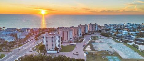 Zona residencial costera con edificios altos, una carretera y un atardecer sobre el océano.