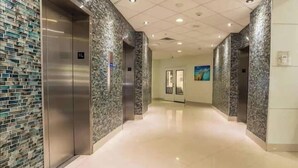 A modern hallway with elevators, a polished floor, and a stone-patterned wall.