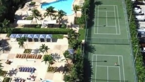 A high-rise hotel with a swimming pool, tennis courts, and sun loungers.
