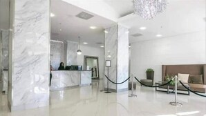 A modern lobby with marble columns, a reception desk, and a seating area with a chandelier.