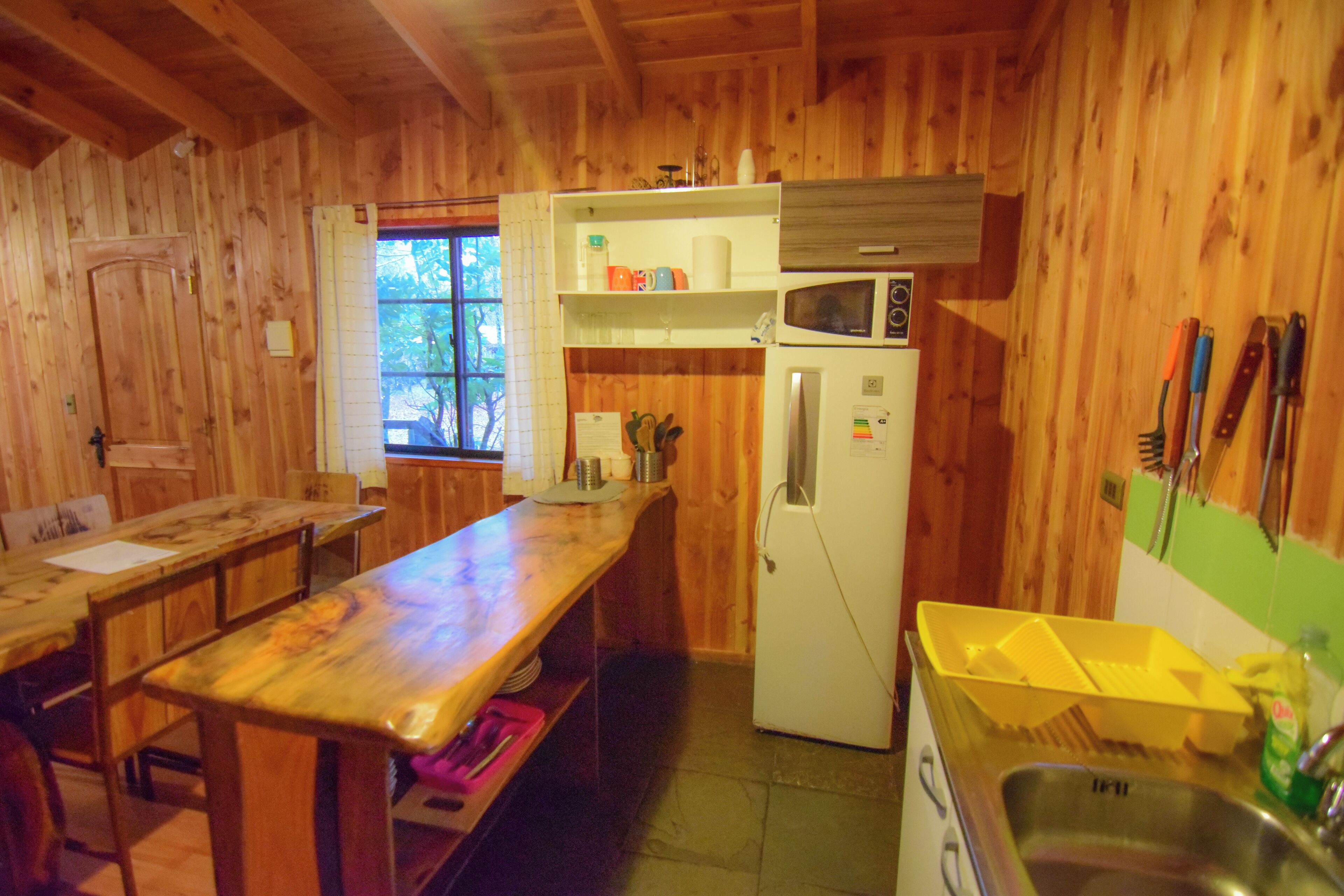 A wooden cabin kitchen with a wooden table, a refrigerator, a microwave, and a sink.