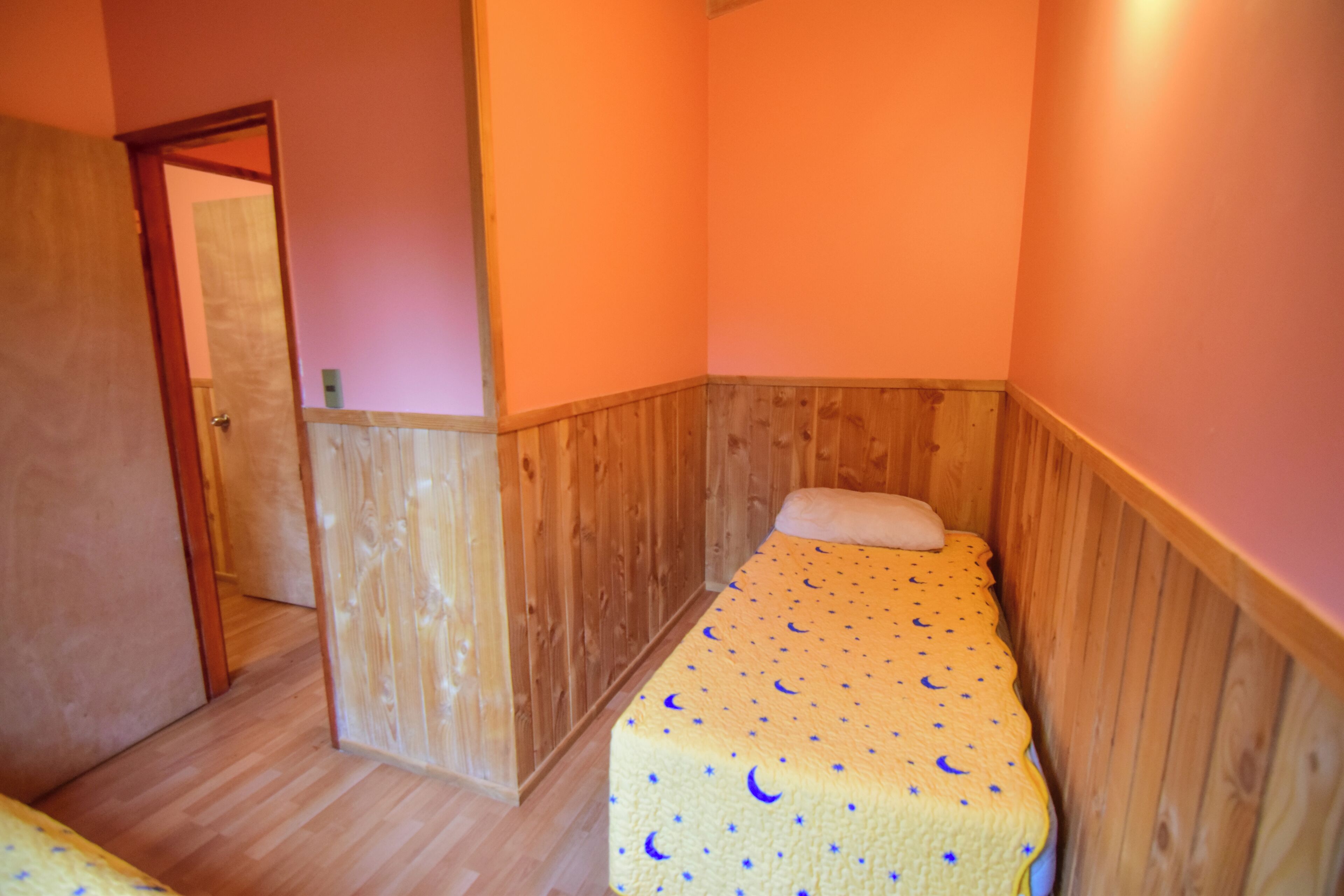 Una habitación pequeña con cama individual, paneles de madera y una colcha amarilla con estampado de estrella y luna creciente.