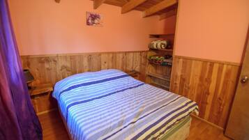 A bedroom with a bed, wooden walls, a shelf with bags, and a door.