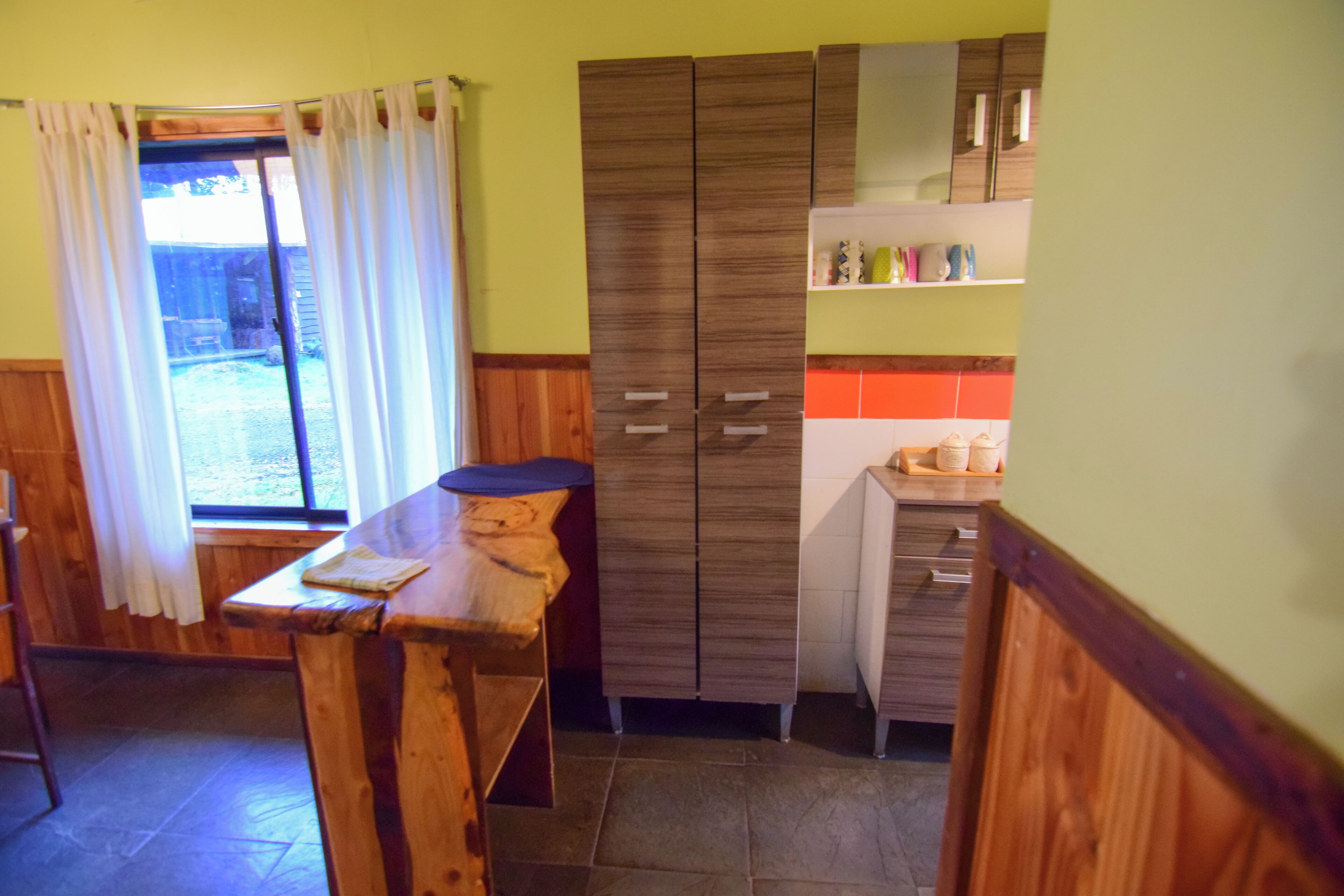 A kitchen with wooden cabinets, a countertop, and a window with curtains.