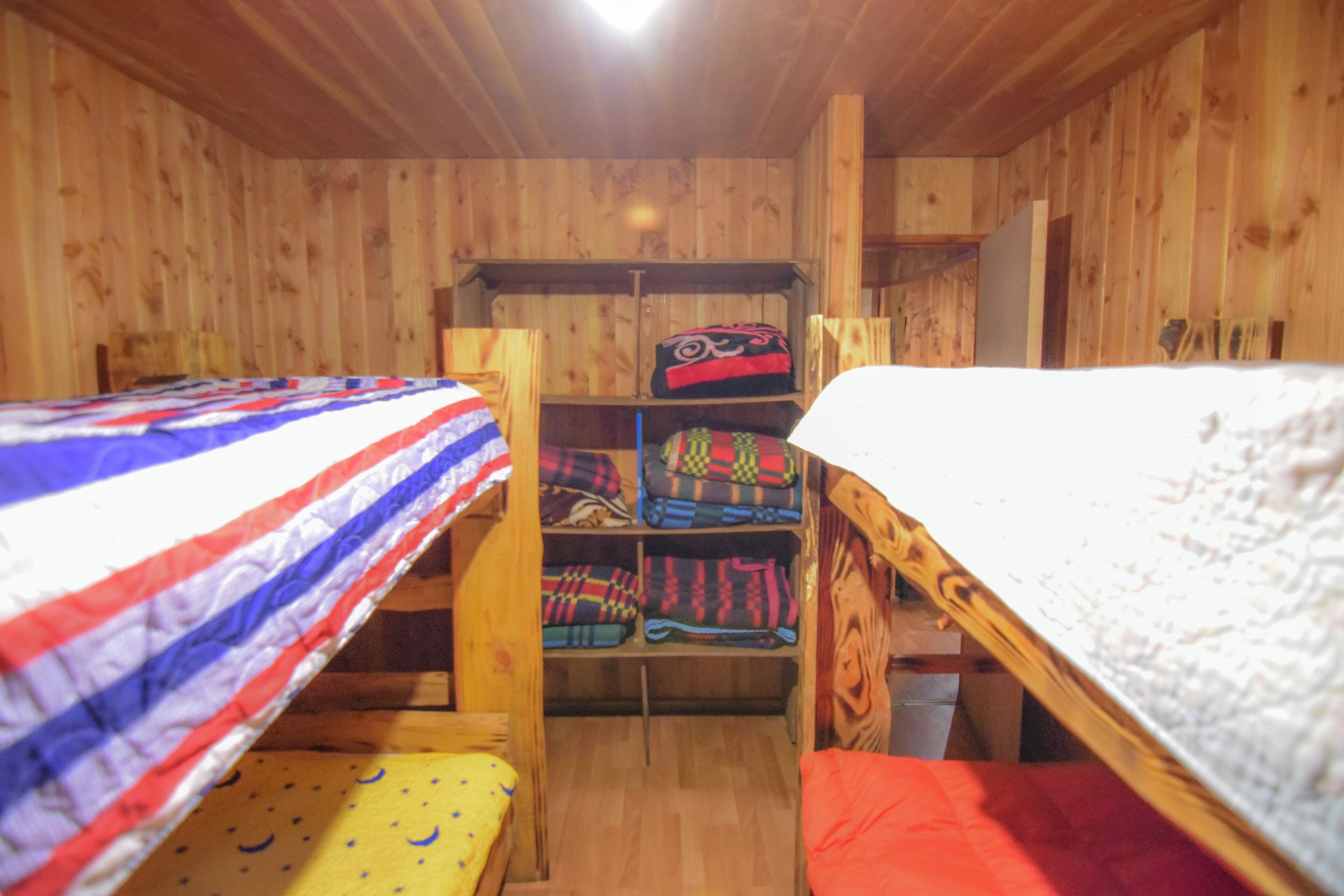 A wooden cabin with bunk beds, a shelf with folded blankets, and a wooden ceiling.