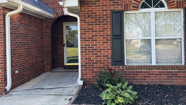 A two-story brick house with a central entrance, a covered porch, and a small garden area.