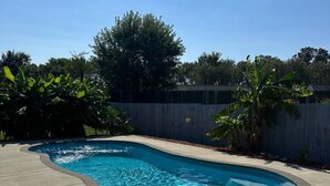 A rectangular swimming pool with a curved edge, surrounded by a concrete deck and a wooden fence.