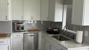 A compact kitchen with white cabinets, a stainless steel dishwasher, a built-in oven, and a sink.
