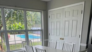 A dining area with a white table and chairs, large windows, and a view of a swimming pool.
