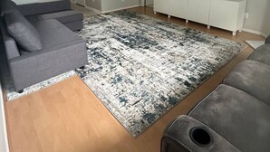 A modern living room with a grey sofa, a patterned rug, a ceiling fan, and a TV on a white cabinet.