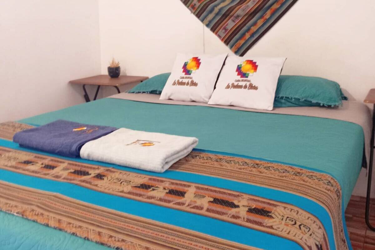 Ein Bett mit einem gemusterten Bettüberzug, zwei Kissen mit farbigem Design und einer blauen Decke.