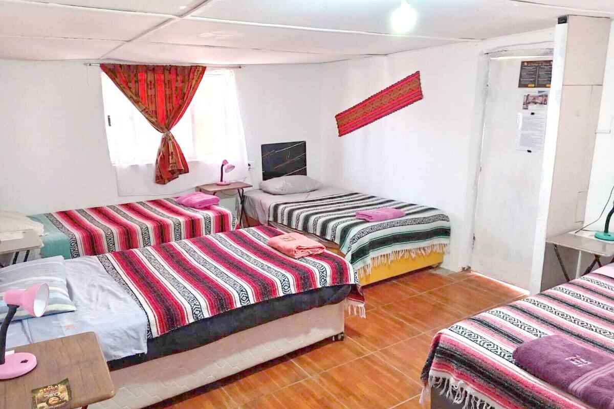 Ein Schlafsaalzimmer mit zwei Betten, einem Schreibtisch, einem Stuhl, einem kleinen Tisch, einem Fernseher und einem Fenster mit Vorhängen.