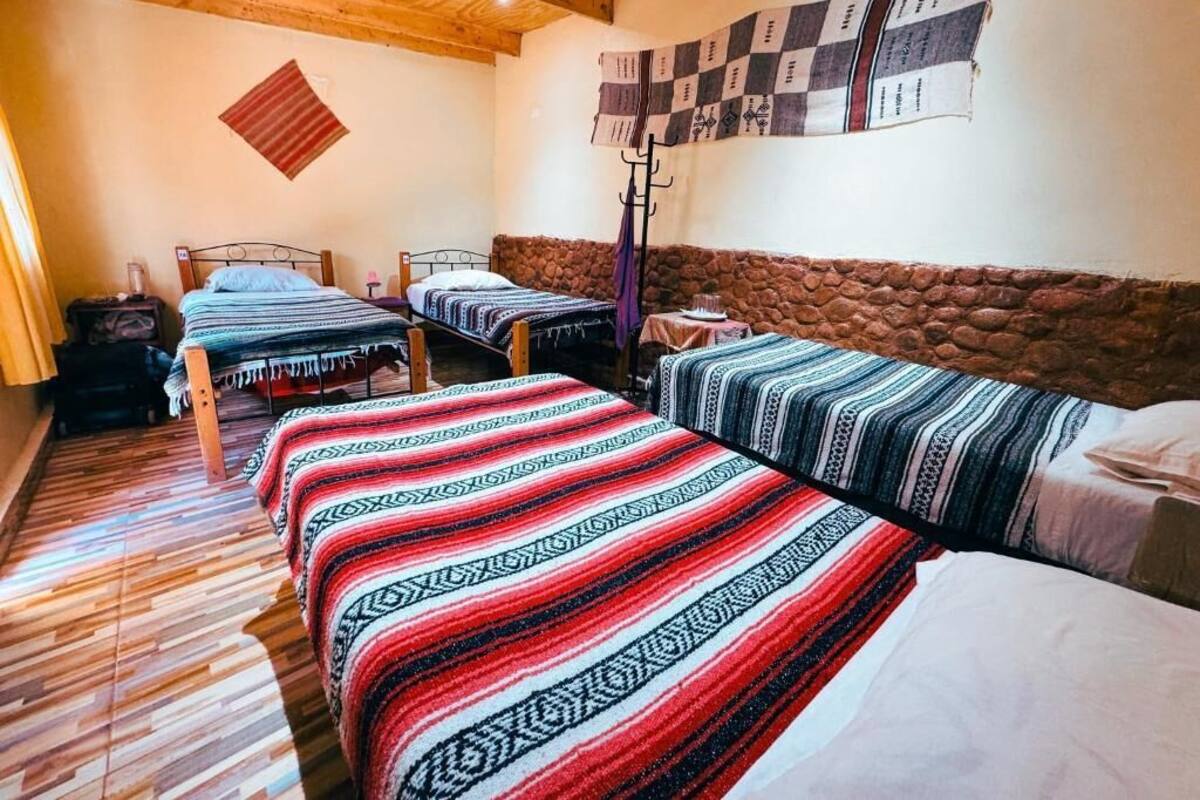 Ein Zimmer mit drei Betten, Holzboden, Steinwand und einer gesteppten Wanddecke.