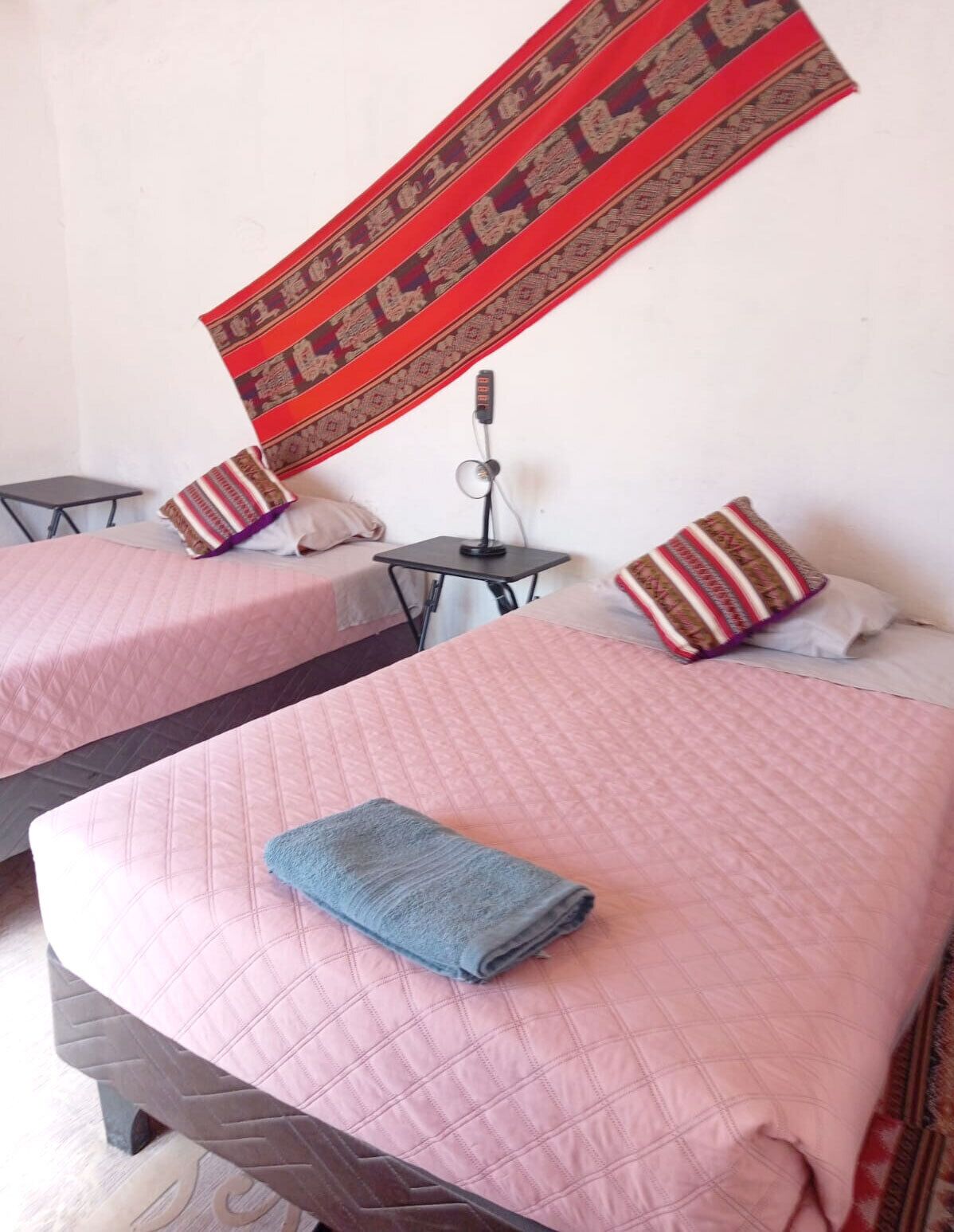 Dos camas con colchas rosas, una mesita con un micrófono y un adorno colgante de diseño rojo y marrón.