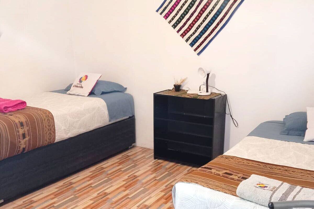 Ein Zimmer mit zwei Betten, einem kleinen schwarzen Nachttisch, Holzboden und einer an der Wand befestigten, gestreiften Dekoration.