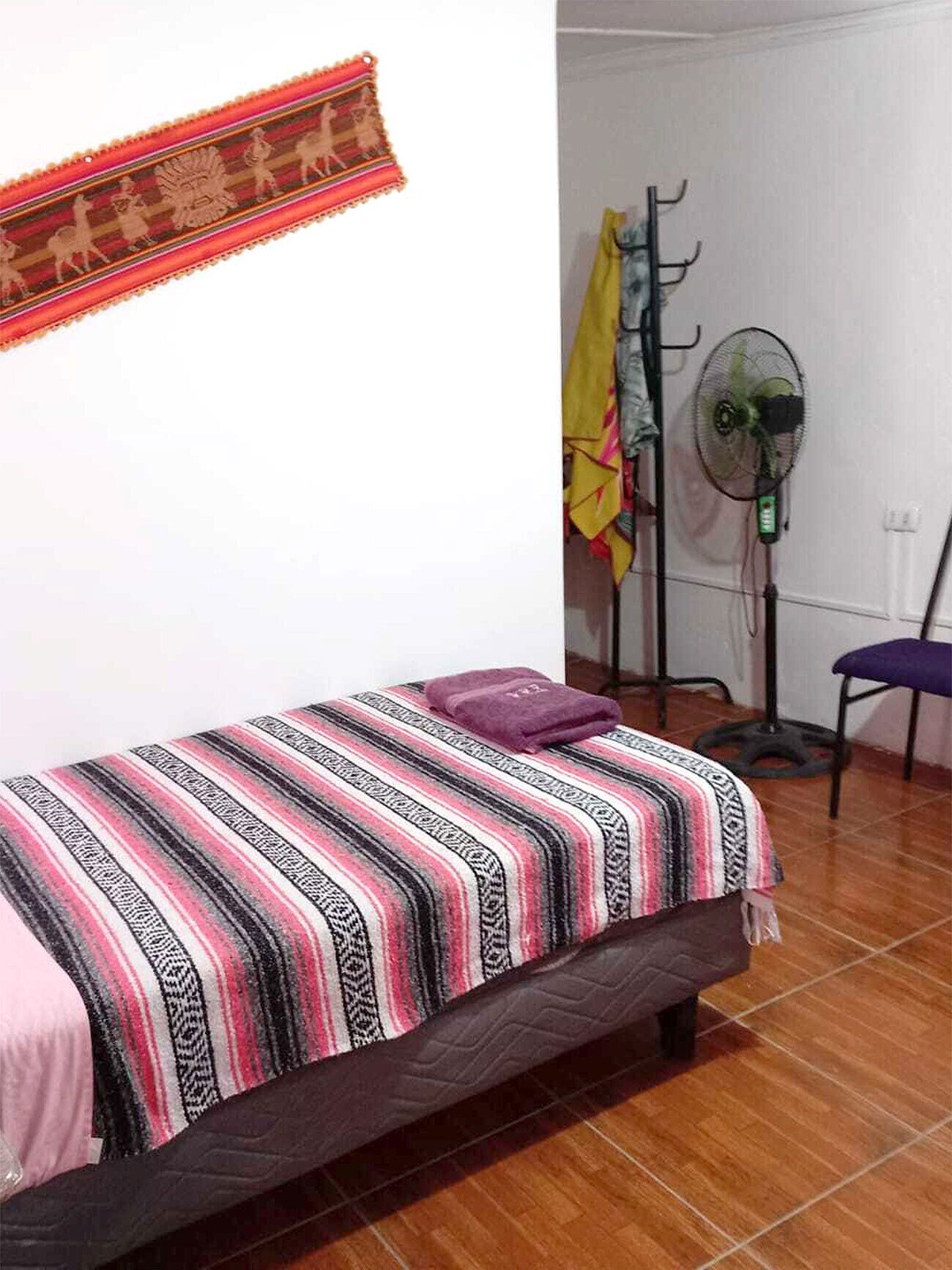 A bedroom with a bed, a wall-mounted fan, and a chair.