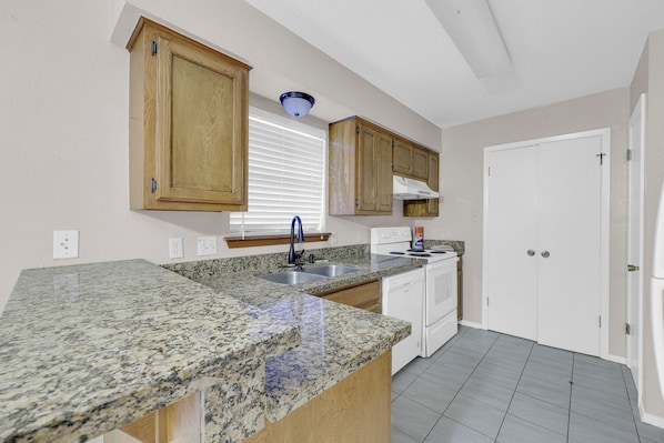 A kitchen with granite countertops, wooden cabinets, a built-in oven, and a white door.
