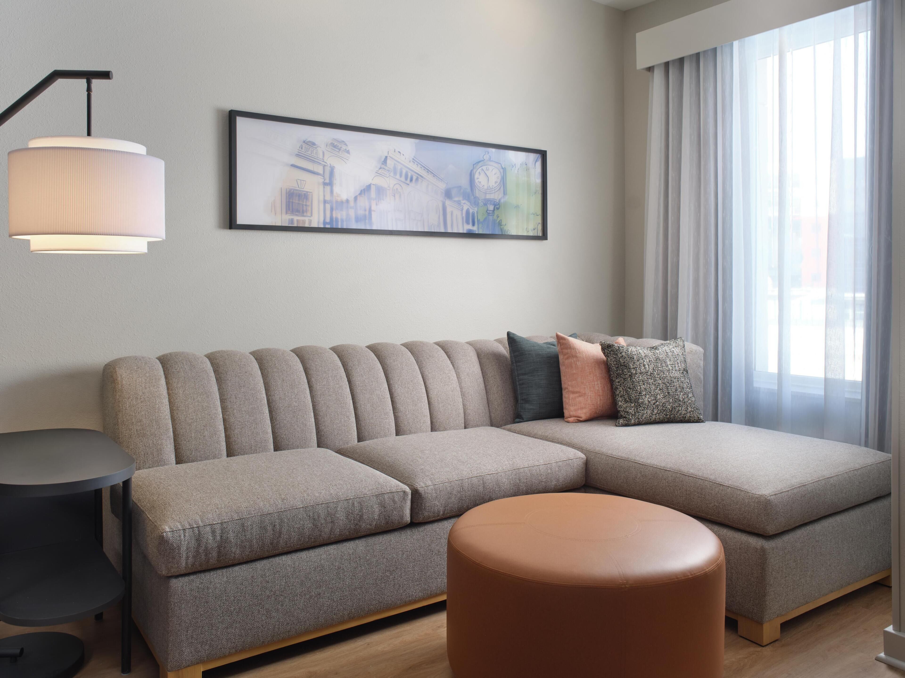 Una sala moderna con un sofá modular, un otoman redondos, una mesita auxiliar y una lámpara de pared.