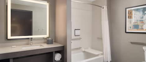 A modern bathroom with a large mirror, a bathtub, a toilet, and a towel rack.