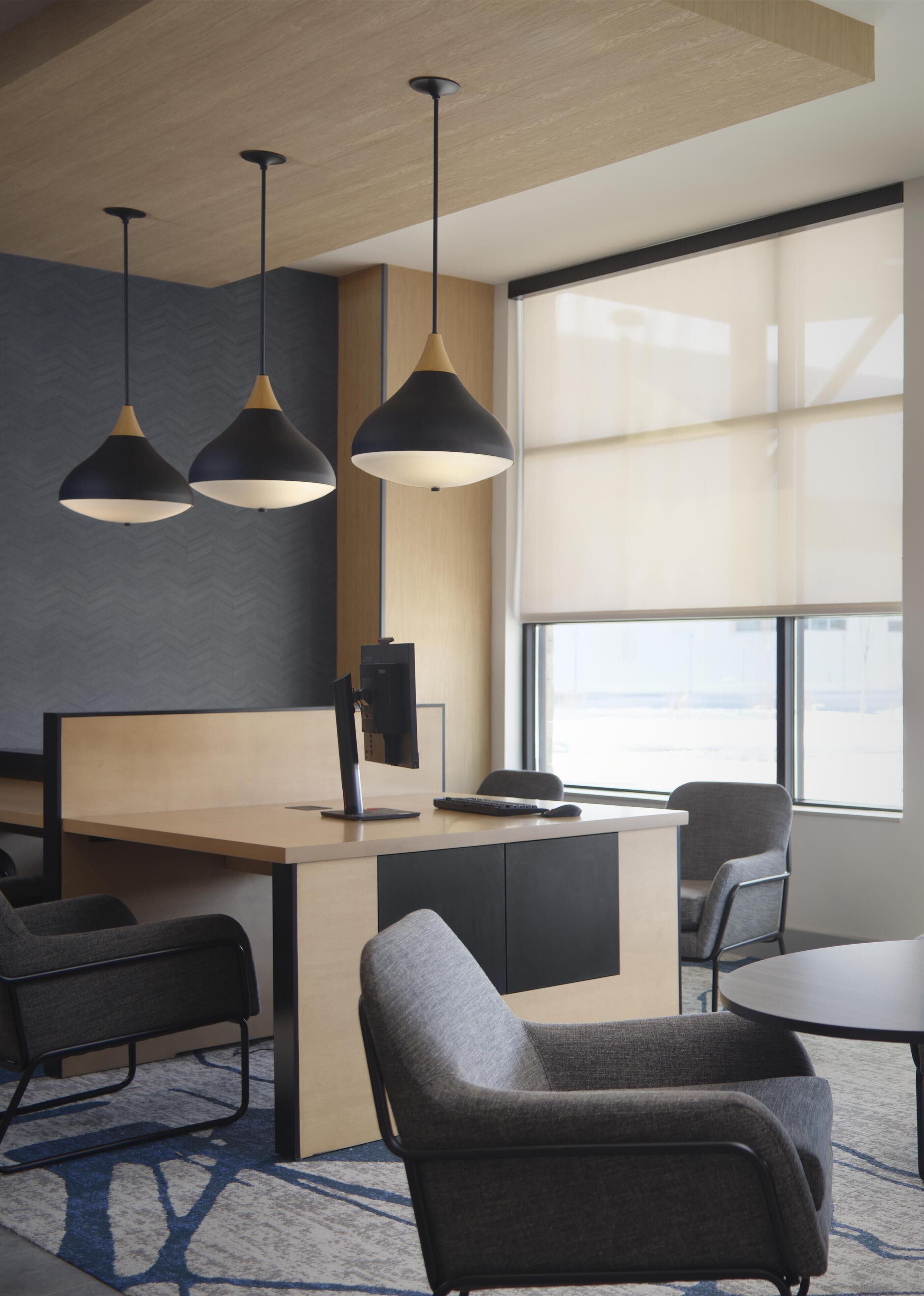 Un espacio de oficina moderno con escritorio, sillas, luces colgantes y un ventanal grande.
