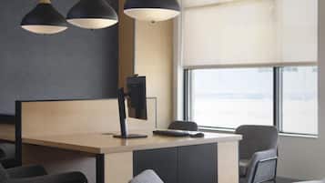 Un espacio de oficina moderno con escritorio, sillas, luces colgantes y un ventanal grande.
