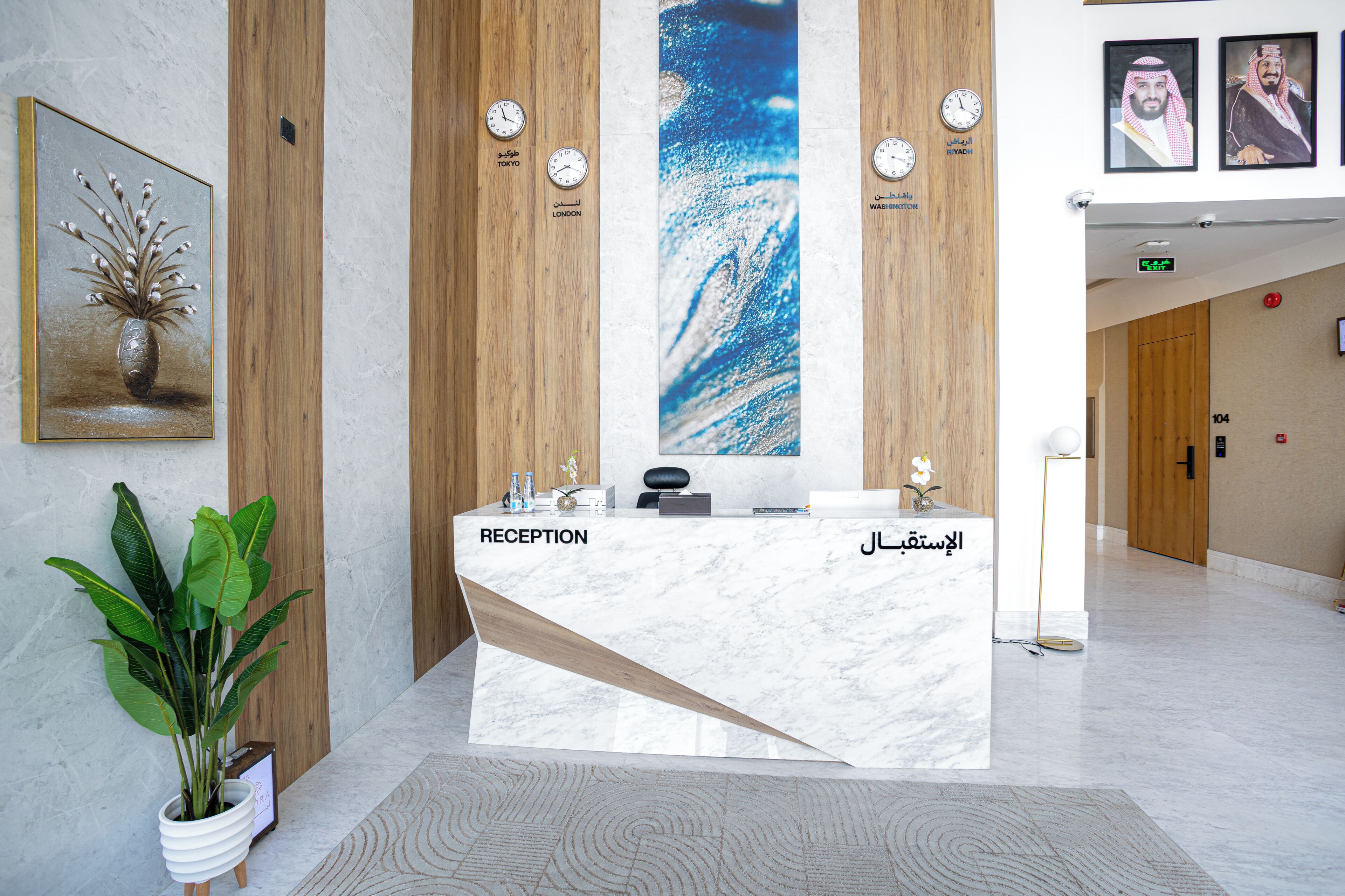 A reception desk with a marble top, a potted plant, and clocks displaying time in multiple languages.