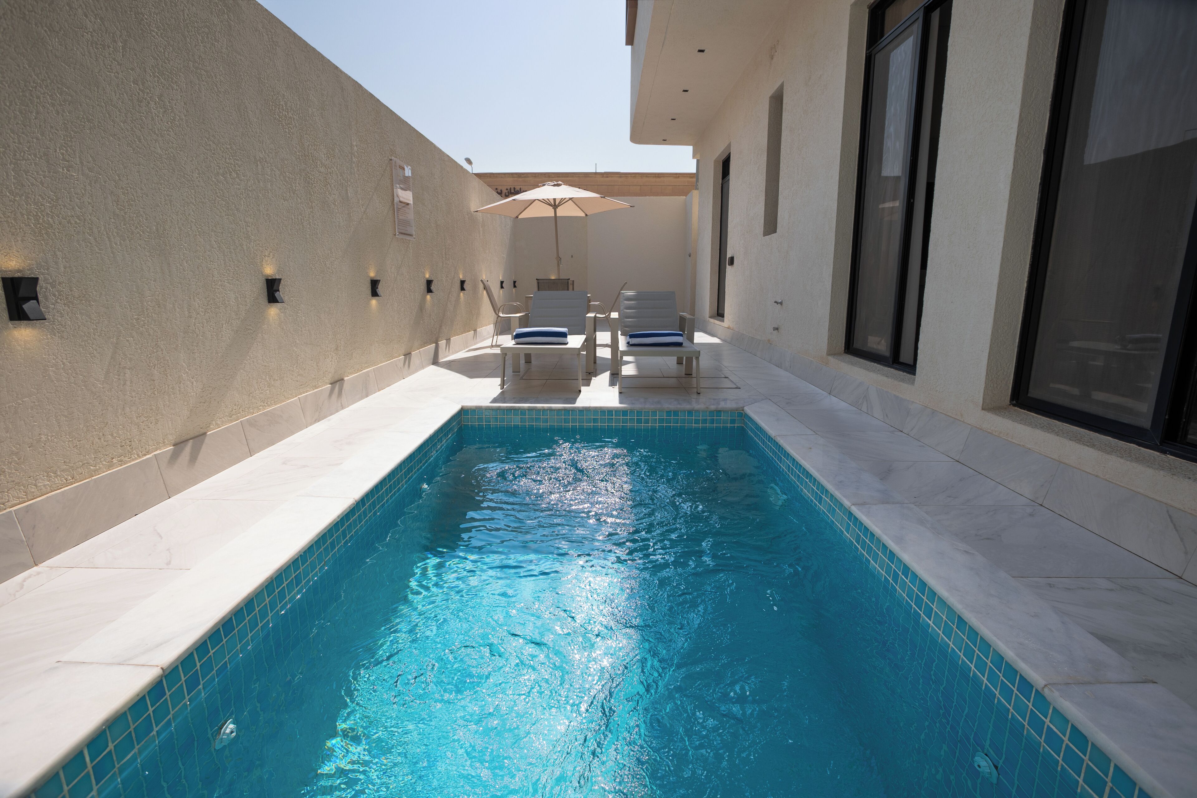 A swimming pool with two lounge chairs and an umbrella, surrounded by a tiled patio area.