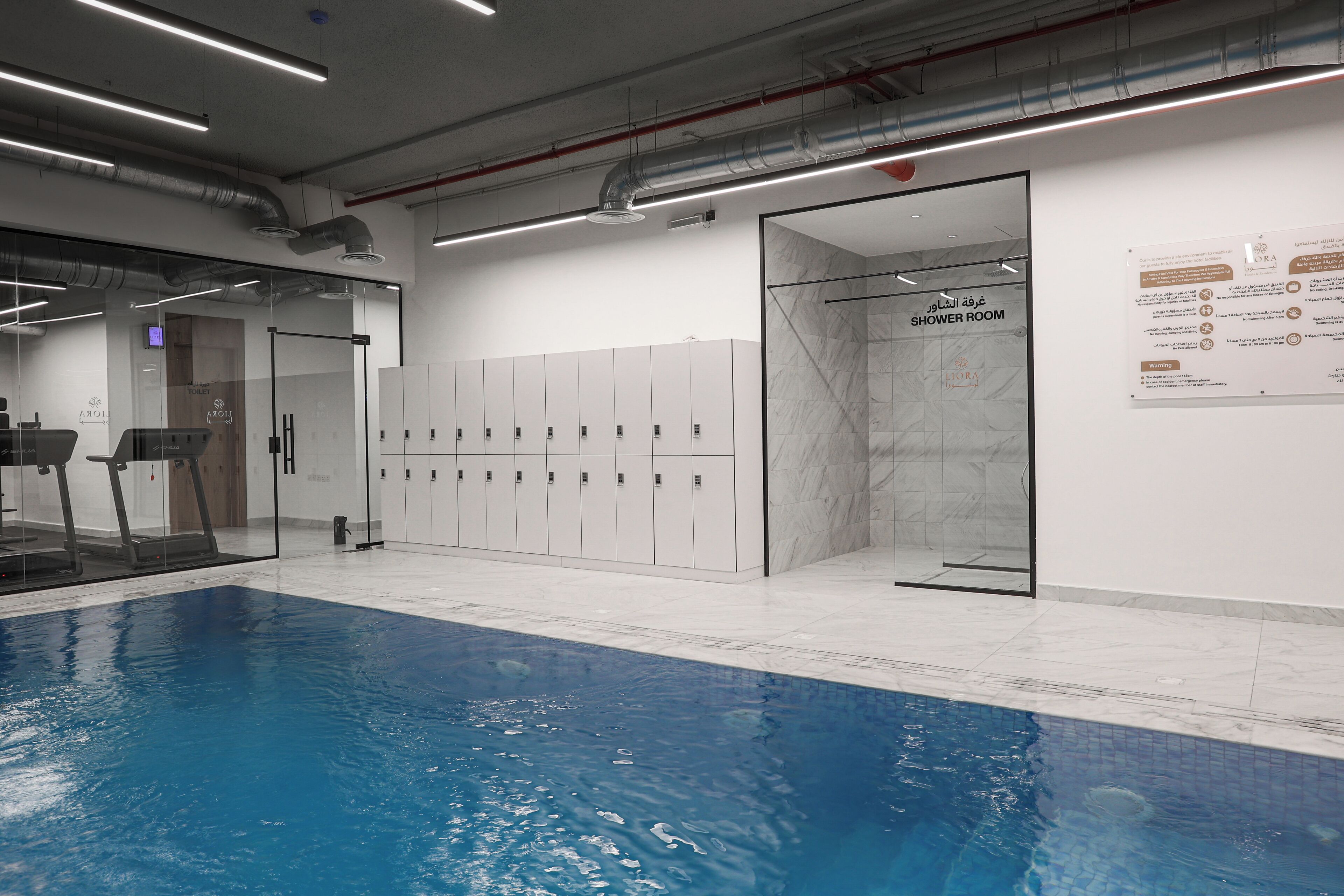 A swimming pool area with lockers, a shower room, and a glass door entrance.