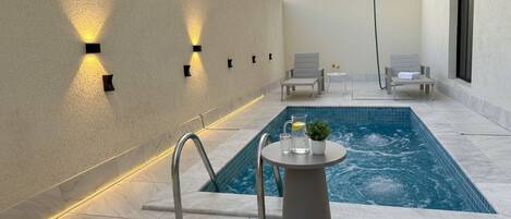 A modern outdoor pool area with a rectangular pool, a small round table with a plant, and two lounge chairs.