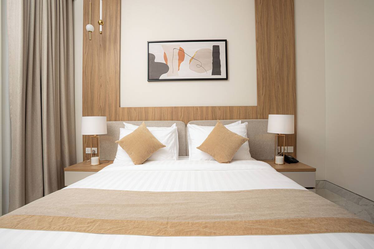 Una habitación de hotel con una cama grande, dos mesitas de noche con lámparas, una obra de arte en la pared y un cabecero de madera.
