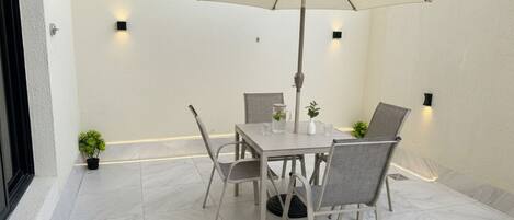 A patio with a table and chairs, an umbrella, and small potted plants.