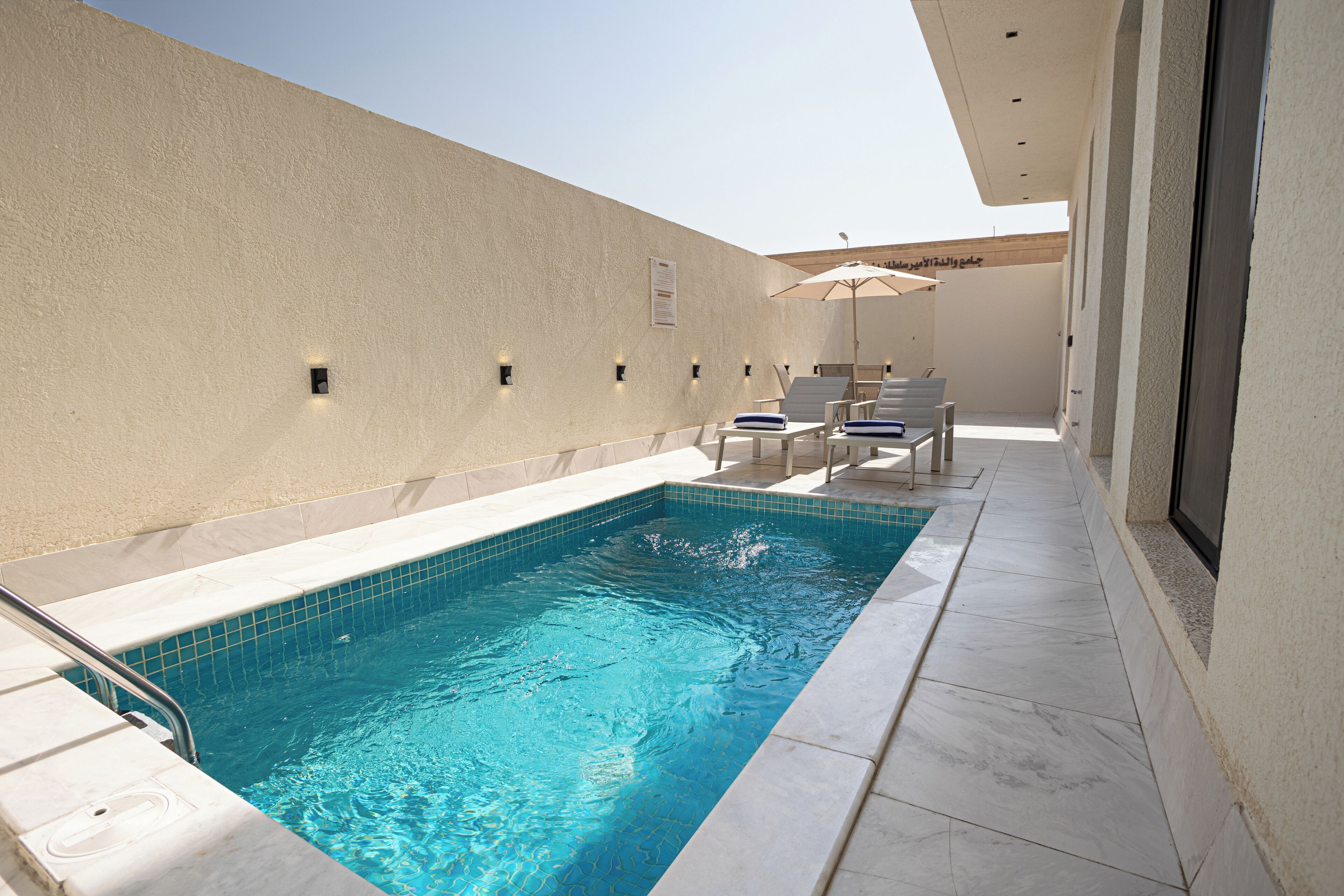 Une piscine avec un bord carrelé, des chaises longues et un parasol.