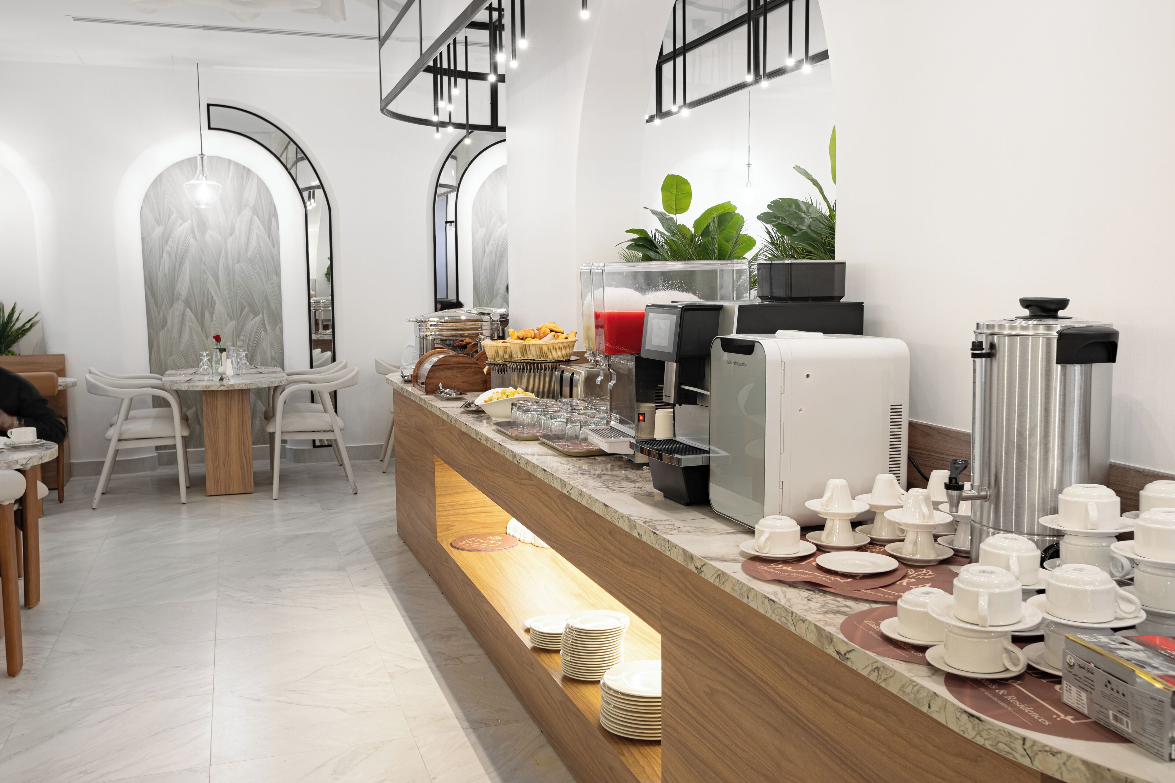 A modern breakfast bar with a marble countertop, coffee machines, and a variety of breakfast items.