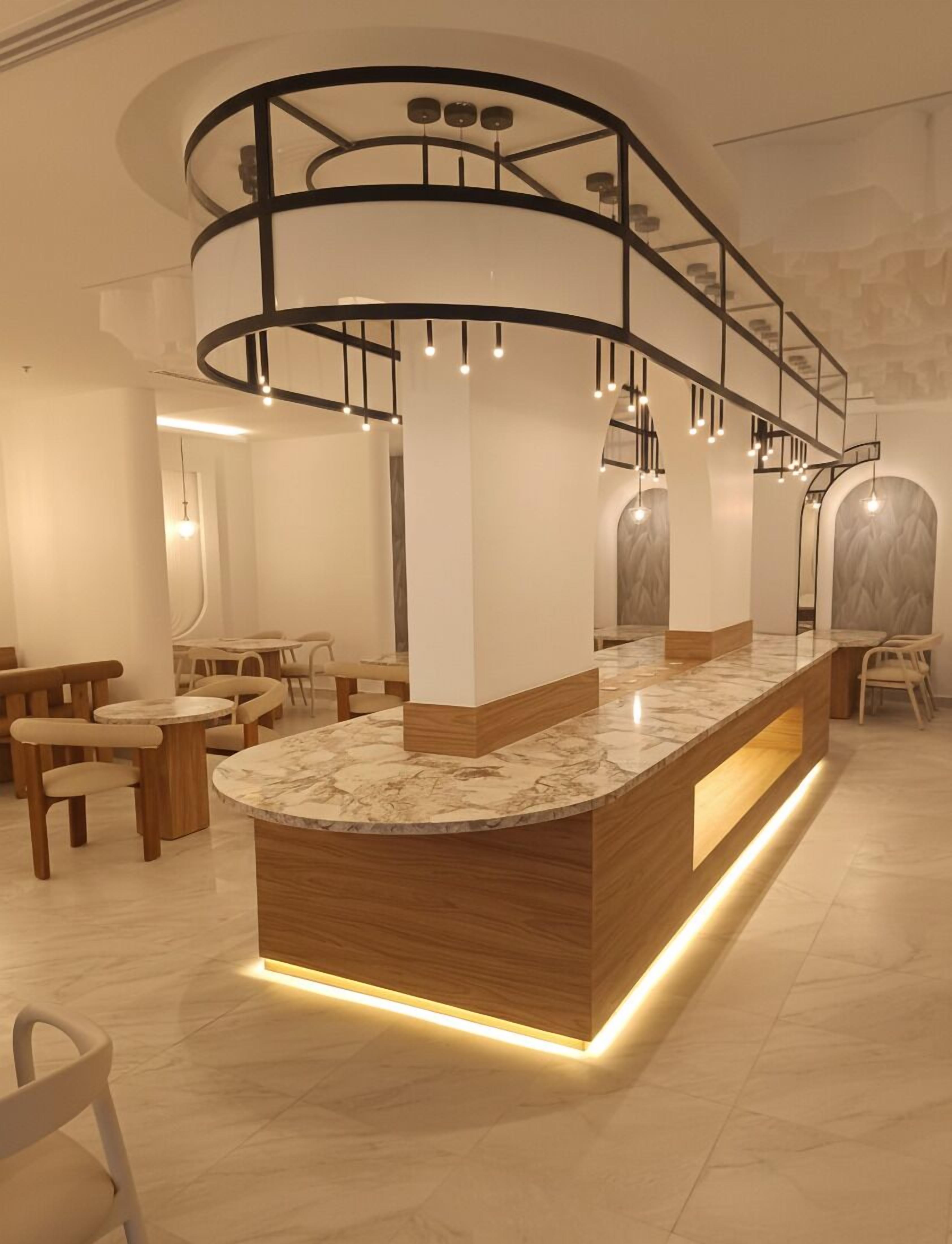 A modern reception area with a marble counter, wooden chairs, and a curved staircase with hanging lights.