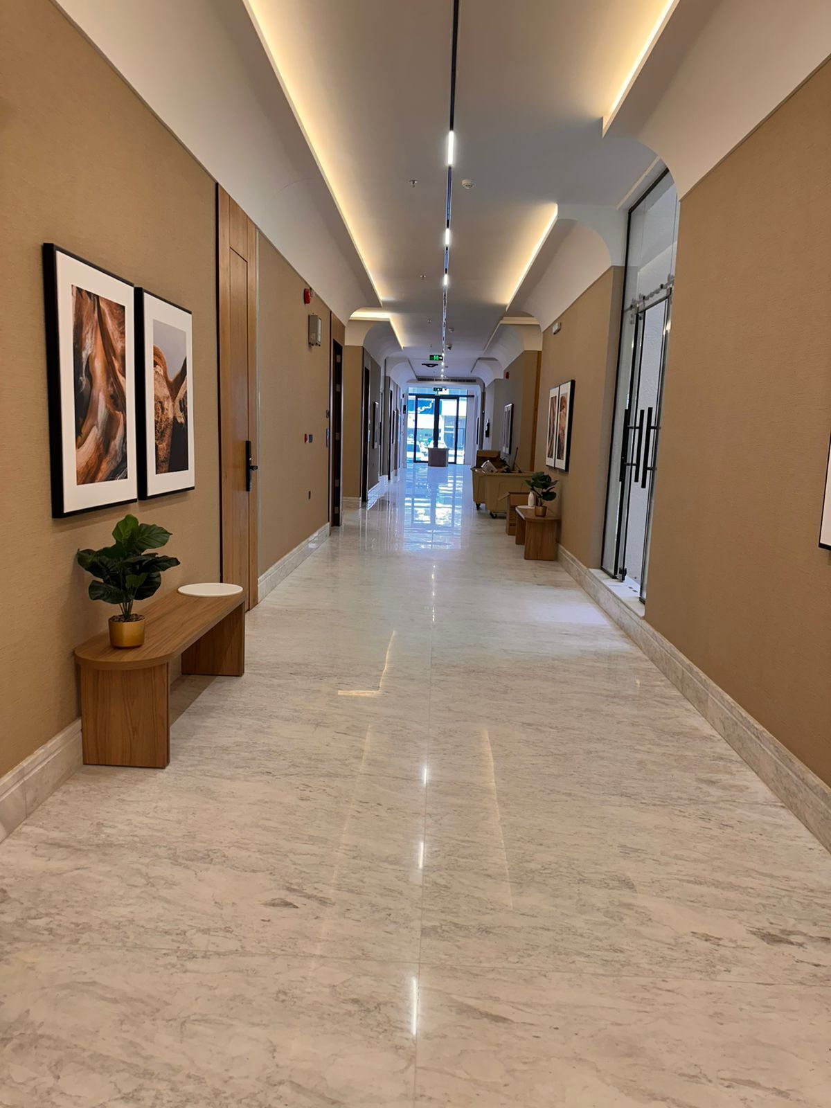 Un pasillo de hotel con pisos de mármol, obras de arte enmarcadas en las paredes y un banco con una planta en maceta.