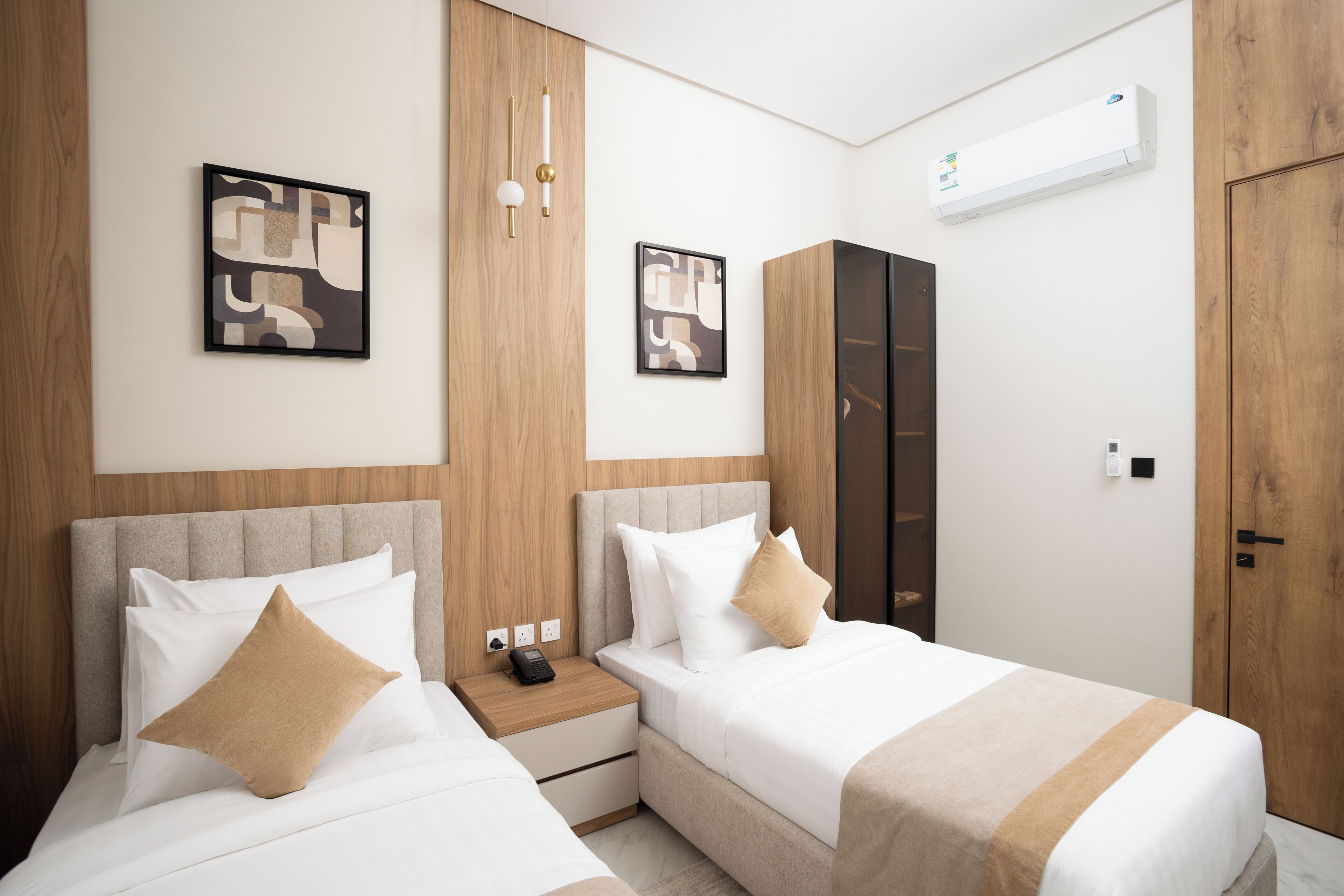 A hotel room with two beds, a wardrobe, and a bedside table with a phone.