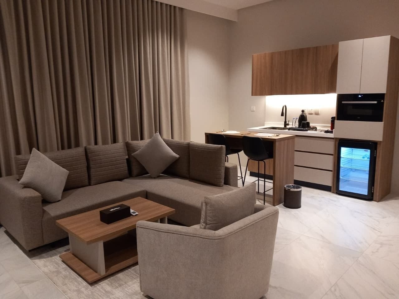 A modern living room with a sectional sofa, a coffee table, and a small dining area with a kitchen in the background.