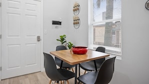 Uma sala de jantar com uma mesa de madeira, cadeiras pretas, uma tigela vermelha e um vaso com planta.
