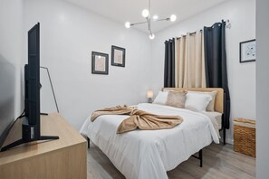 A modern bedroom with a bed, a TV on a stand, and a ceiling light fixture. - Cocoa - Springfield Brand NEW Apt! (Jacksonville)