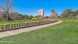 Um parque com um caminho pavimentado, um edifício alto ao fundo e um céu azul e límpido.