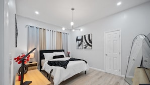 Quarto moderno com cama, mesa de cabeceira, luminária e obra de arte.