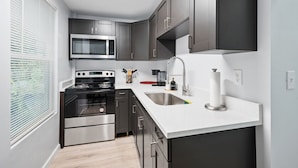 Cozinha moderna com armários escuros, eletrodomésticos de aço inoxidável e bancada branca.