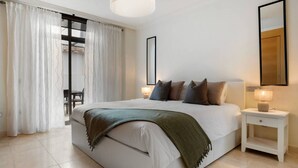 Ein modernes Hotelzimmer mit einem großen Bett, einem Nachttisch mit Lampe und Blick ins Freie durch ein Fenster mit Vorhängen.