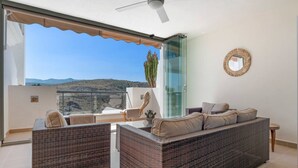 Ein Balkon mit Korbmöbeln, einer Glastür und Blick auf die Landschaft.