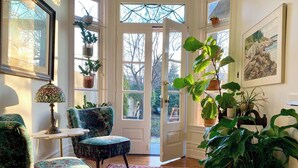Una habitación acogedora con un sillón estampado, una mesita pequeña, un tapete colorido y varias plantas en macetas.