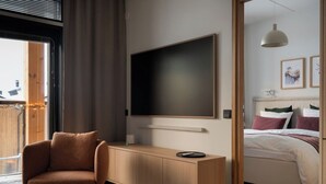 Un dormitorio moderno con cama, escritorio, silla y un televisor grande.